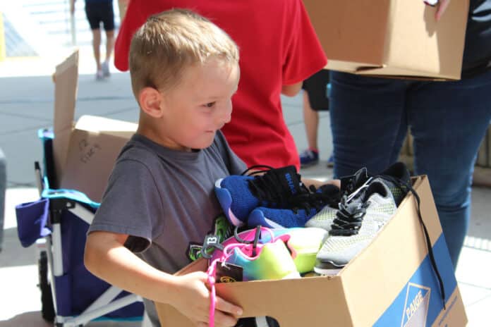 One tiny student carries a big box of shoes donated by SWFWMD to the picnic tables.