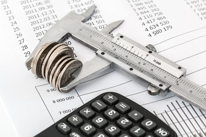 Image of a budget sheet with a calculator and coins squeezed in a caliper