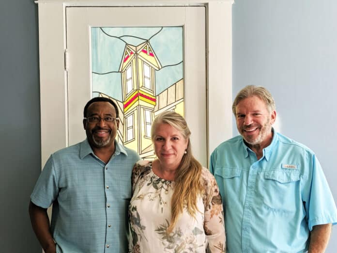 ABOVE: From left to right, Gerald Johnson, Kala Johnston and Ken McCullick stand in front of a stained glass by Susan Healy depicting the historic home.  Gerald and Kala have been restoring the home for a year and a half.  