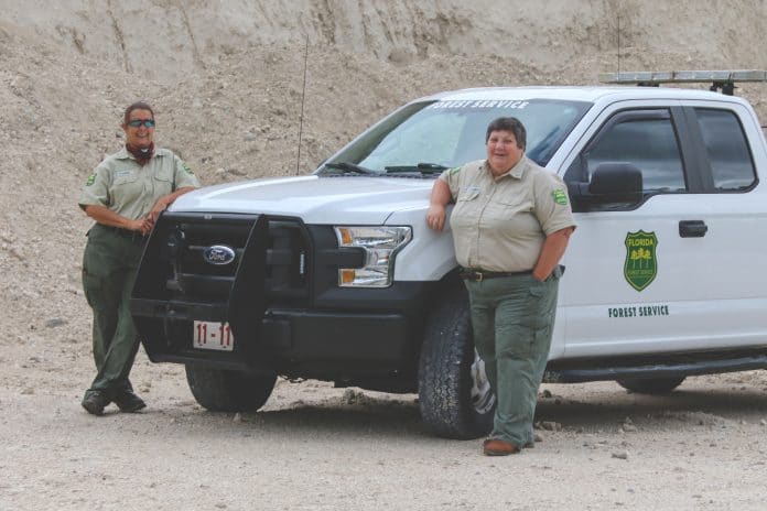 Cherie Plourde, Road Crew Staff (left), and Gerri Velazquez, Facility Maintenance Administrator in front of the limestone piles used for road work. 