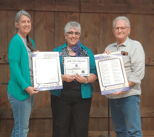 Stable Faith Cowboy Church Program Coordinator Valerie Ansell, left, and Pastor David Hope, right, receive Dementia Friendly certification documents from Coping with Dementia LLC President Debbie Selsavage.