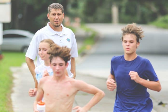 Hernando High’s Cross Country coach Travis Bruns hands runner Jesse Foulks a water bottle during a practice run near Hernando High School on August 16. 