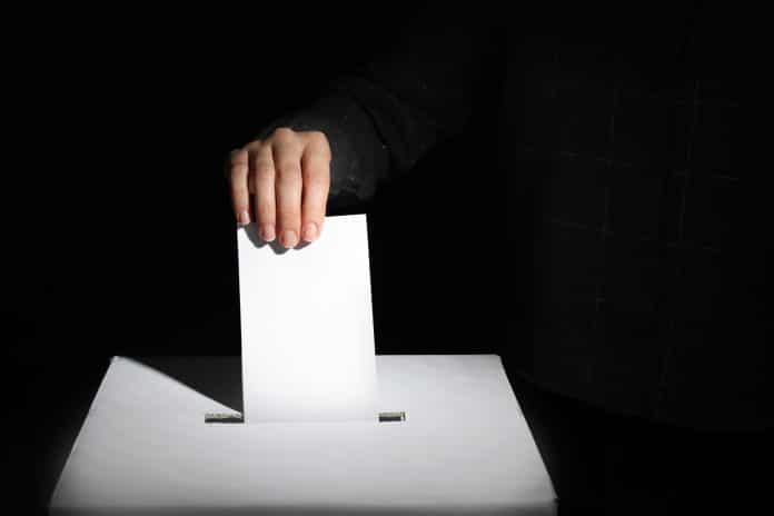 Voting woman near ballot box on dark background