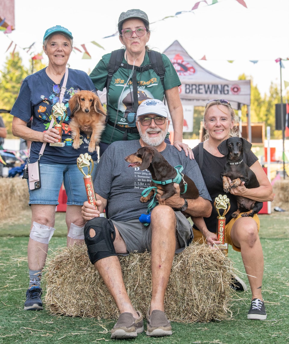 2022 Marker 48, “Running of the Wieners” Winner Sofia, center, with owners Eleanor, standing center and Tom Smith seated, Second Placer, Winston with owner Shelly Pevarnick on right and Third place, Molly and her owner Janice VanOss, left. Photo by JOE DiCRISTOFALO.