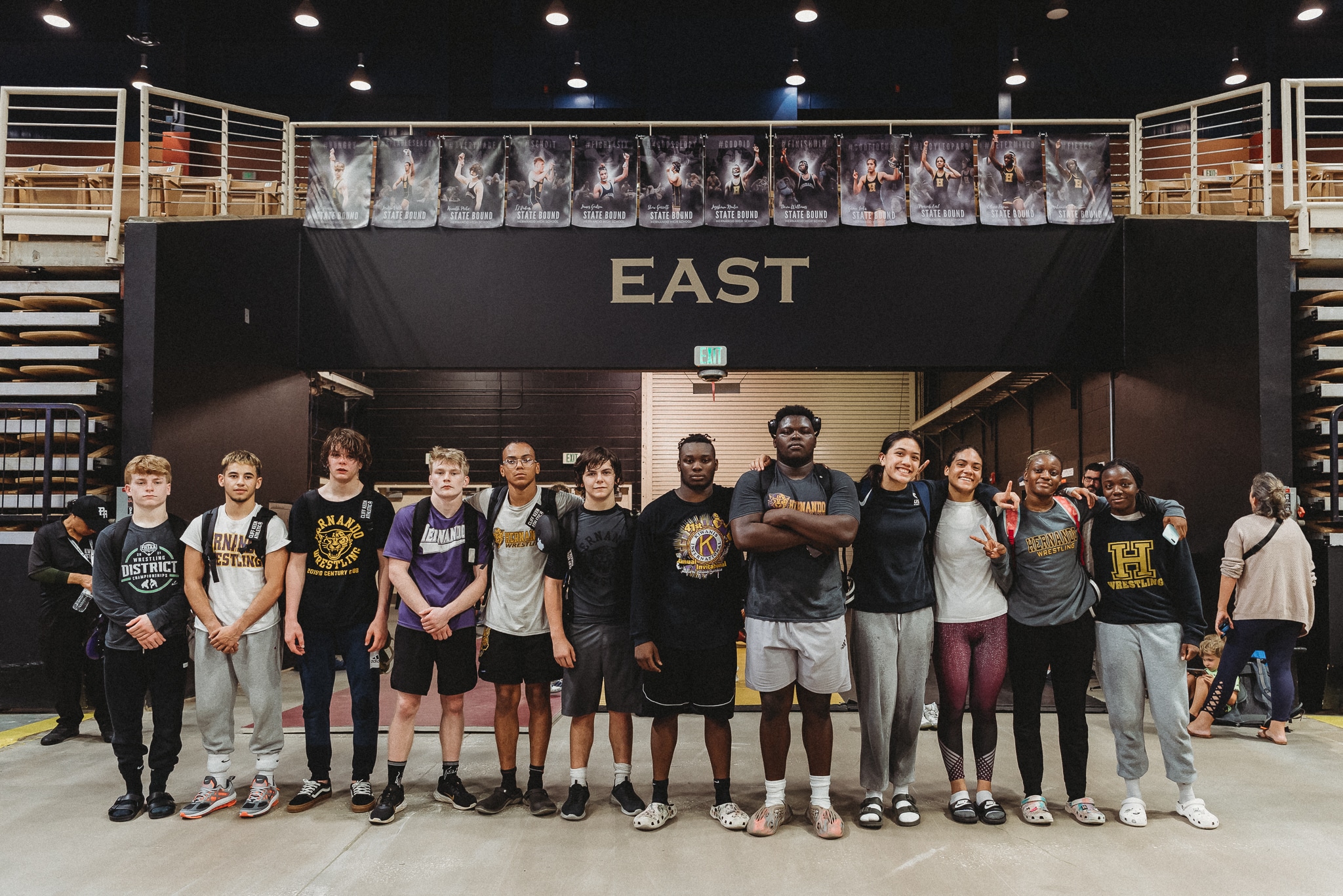 Hernando High School State Wrestling Qualifiers pose beneath their banners at Silver Spurs Arena. Left to Right: Kyle Pearson, Jordyn Valle, Kenneth Pritz, TJ Rodier, James Gadson, Shaw Garrett, Jayshawn Nantce, Devin Williams, Grace Leota, Mariah Earl, Olivia Brown, and Makenzie Eltzroth.