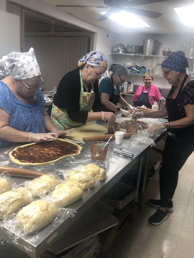 The dough has been rolled using a French rolling pin. The cinnamon filling is being spread on the dough and will will then be folded. From left to right around the table: Debra, Jan, Carla, Cookie and Gayle.