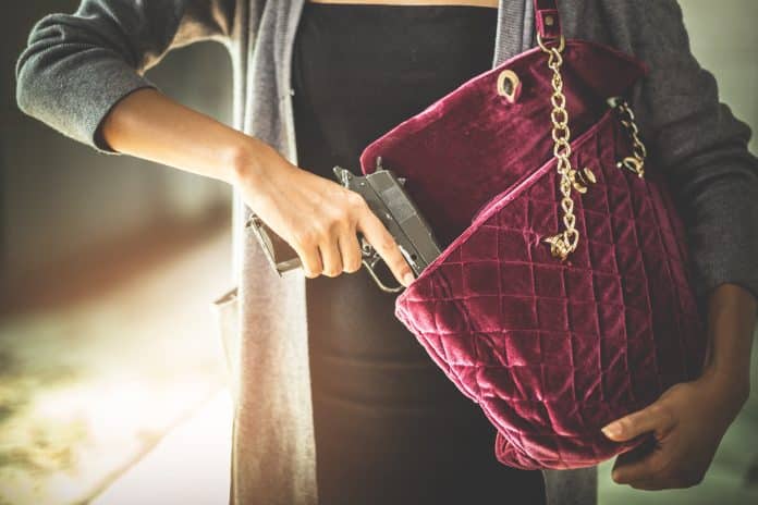 Woman pulls a gun from her purse. Conceal carry weapon for protection themselves concept. Selective focus to gun.