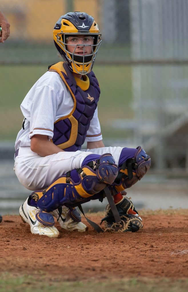 Hernando High catcher, Drew Bittenger , looks into the dugout for a pitch sign during Friday night’s game with Lecanto High. Photo by JOE DiCRISTOFALO