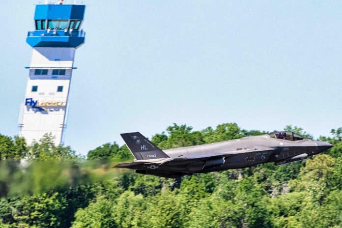 A USAF F-35 Lightning II, flown by Major Kristin “Beo” Wolfe makes a high-speed pass in front of the control tower, appearing to take the tower with her. Photo credit: Mark Stone