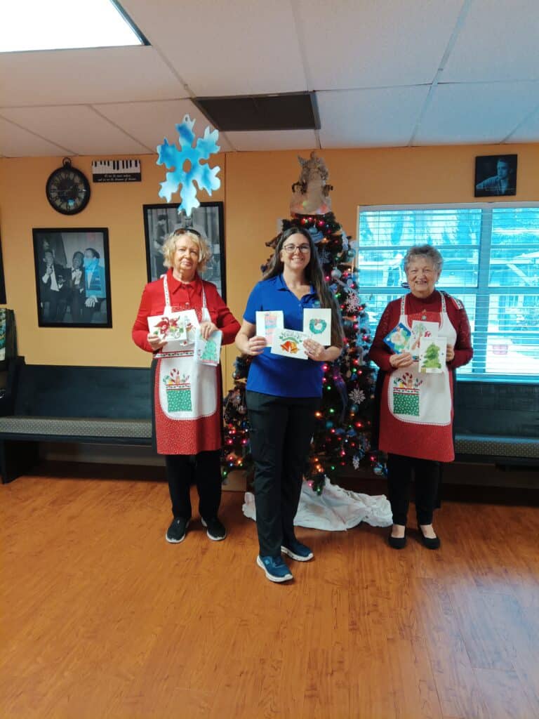 Bonnie Young and Linda Graves, Nature Coast Art League members, joined Brooksville Healthcare Center Activities Director Kara Hazivasilis in spearheading the Nature Coast Art League Christmas Card art project. [Credit: G. Valentin]