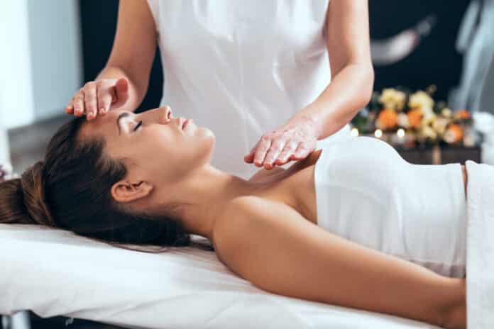 Shot of beautiful young woman having reiki healing treatment in health spa center.