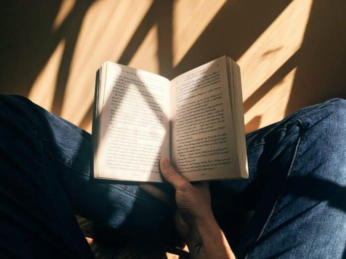 Person holding book sitting on brown surface. [Photo by Blaz Photo on Unsplash]