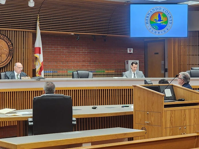 Warnstadt (far left), Peters (left), and Frank Bierwiler (far right) discuss the pool contractor’s outstanding permits at Wednesday’s special master hearing. [Credit: A. Szempruch]