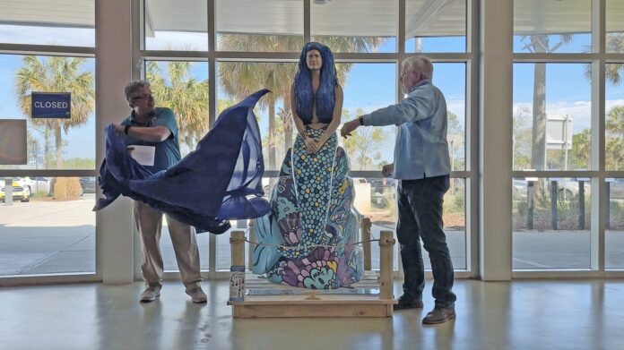 At a Feb. 15 unveiling ceremony, John Athanason, a tourism marketing specialist with Florida’s Adventure Coast Visitors Bureau, joined David Dodd, Visit Florida Welcome Center, in revealing the Tail Trail statue Meraki to center visitors. [Photo supplied by Florida's Adventure Coast Visitors Bureau]