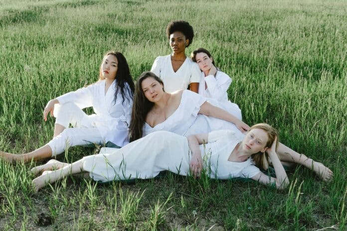 Group of women in white clothing laying on grass.