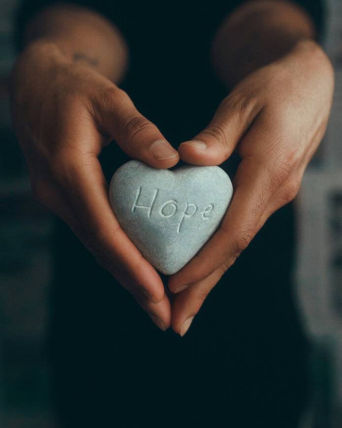 Woman's hands holding a heart-shaped rock with the word 