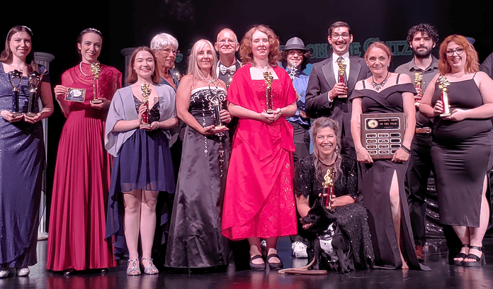 (L-R) Front Row – Jennifer Scalf (purple dress), Victoria Zisi (red dress), Shawna Hopper, Toni Dwyer, Jessica Haberland, Char Adams (kneeling ), Capt. Jack Friel (dog), Michelle root, Kristin Nelson; Back row – Lynda Dilts-Benson, Jay Ingle, Journey Weeks, Kristoff Stens, Zachary Smith [Photo by Sarah Nachin]