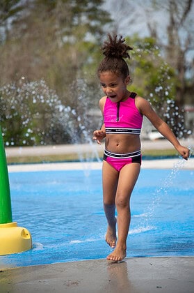 A little girl avoids the cold water spray at the grand opening of the splash pad at Tom Varn Park on March 1, 2025. [Photo by Jenifer Truitt]