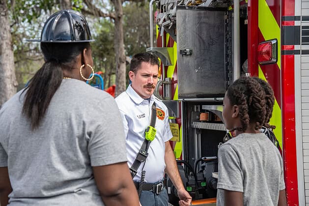 Fire Captain Palmieri teaches a local boy about a career in firefighting at the Tom Varn Park splash pad grand opening on March 1, 2025. [Photo by Jenifer Truitt]